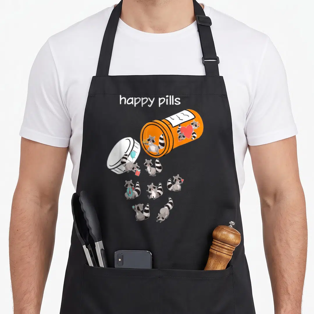 Pill funny raccoon lover apron - Orange pill bottle spilling cartoon raccoons holding balloons, gifts, and hearts — shown on a black cotton canvas apron against a white background