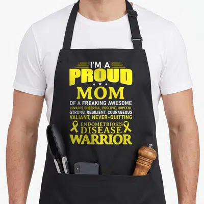 Endometriosis disease ribbon apron - Yellow text reading proud mom endometriosis disease warrior with three stars — shown on a black cotton canvas apron against a white background