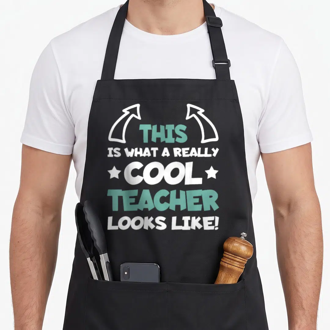 Teaching student teacher apron - Stacked text reading This Is What A Really Cool Teacher Looks Like with arrows — shown on a black cotton canvas apron against a white background