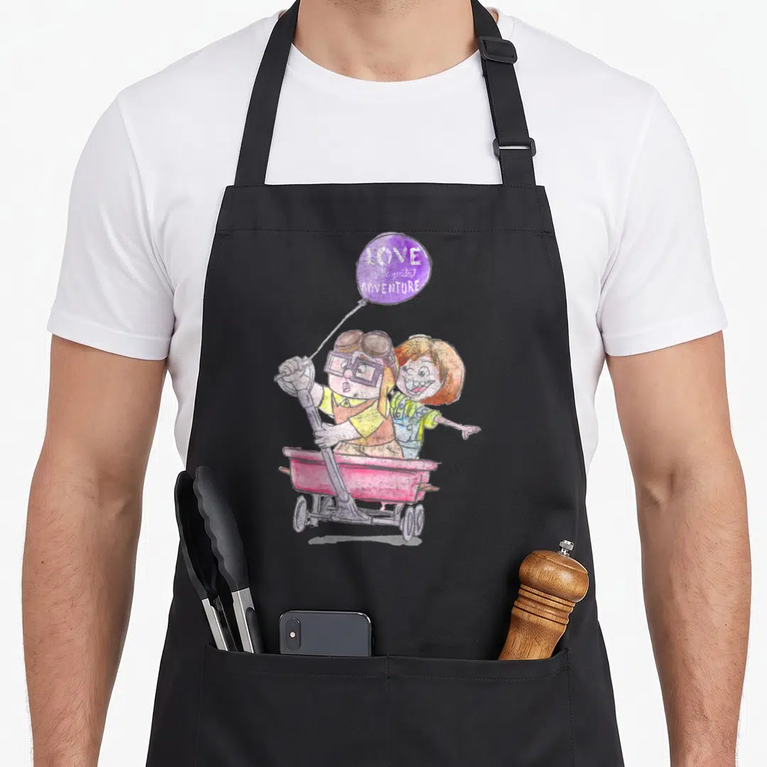 Wagon carl and ellie apron - Two children in pink wagon holding purple balloon with LOVE is the greatest ADVENTURE text — shown on a black cotton canvas apron against a white background