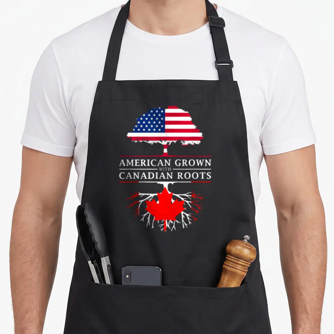 Grown canadian aprons - Tree split by text with US flag canopy and Canadian maple leaf roots in red white blue — shown on a black cotton canvas apron against a white background