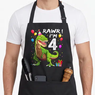 4th t-rex apron - Green T-Rex in party hat with RAWR I'M 4 text, balloons, and presents — shown on a black cotton canvas apron against a white background