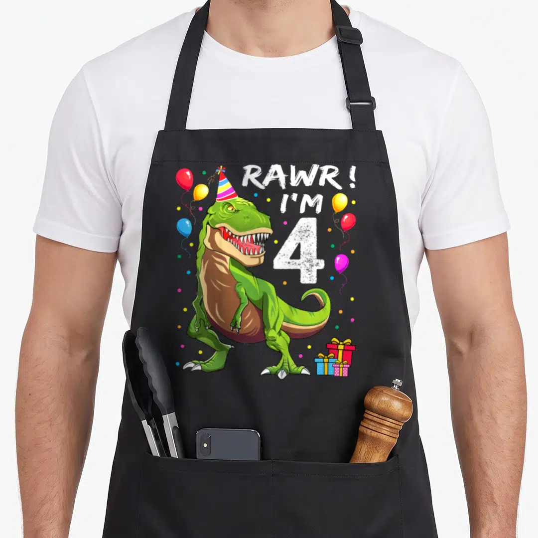 4th t-rex apron - Green T-Rex in party hat with RAWR I'M 4 text, balloons, and presents — shown on a black cotton canvas apron against a white background