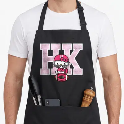 Education football apron - Hello Kitty in pink helmet sits on football below large pink HK letters — shown on a black cotton canvas apron against a white background