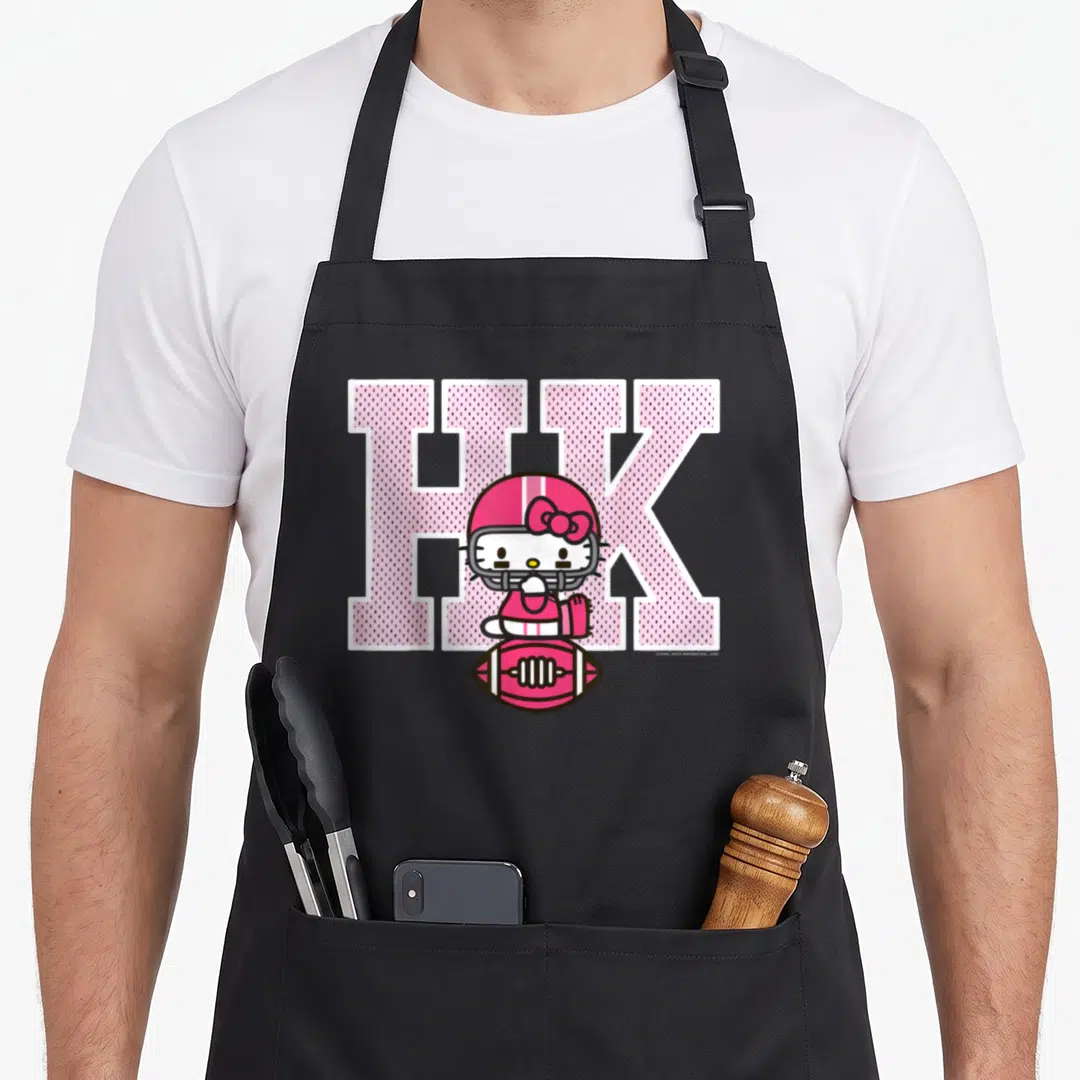 Education football apron - Hello Kitty in pink helmet sits on football below large pink HK letters — shown on a black cotton canvas apron against a white background