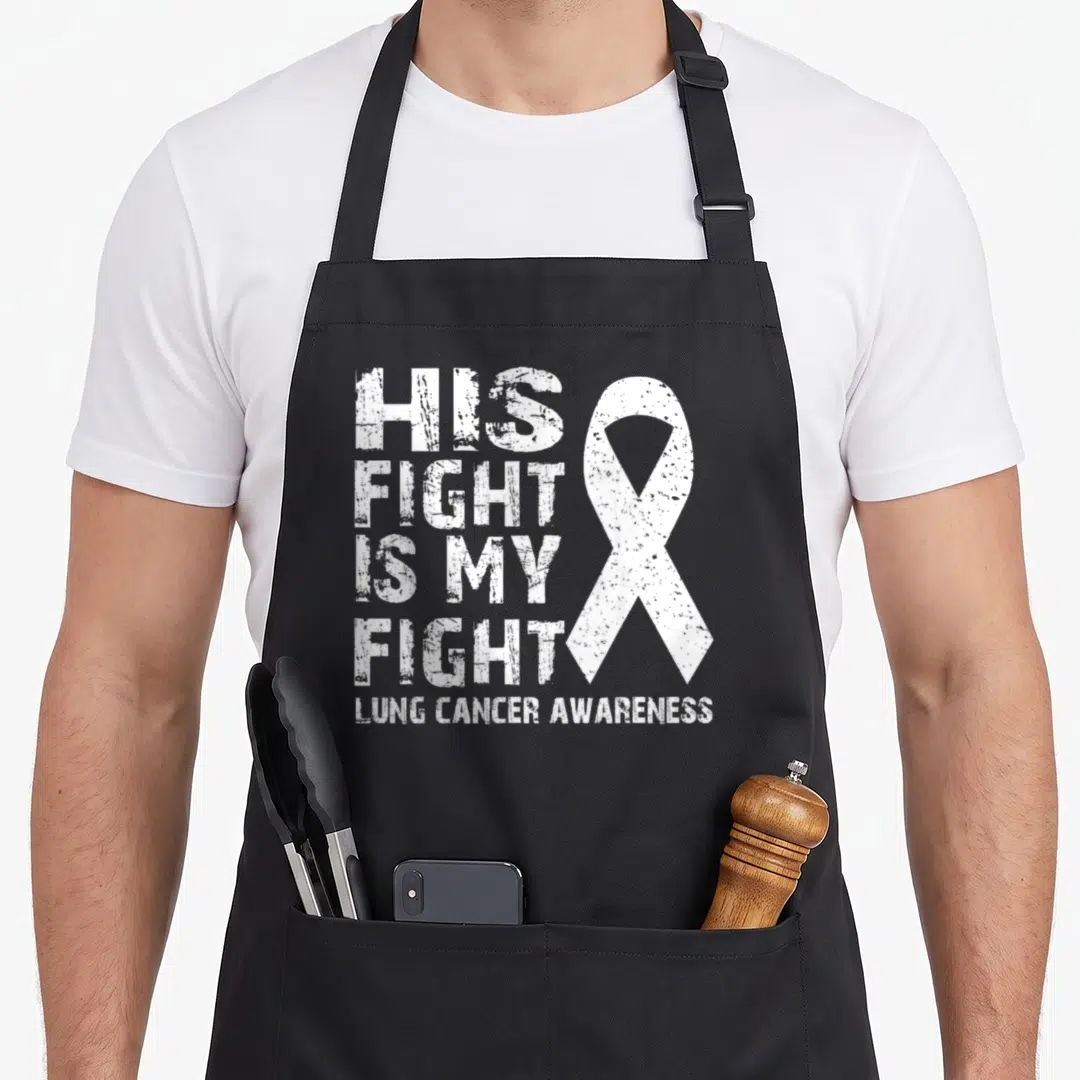 His cancer girl apron - White distressed text His Fight Is My Fight next to an awareness ribbon — shown on a black cotton canvas apron against a white background