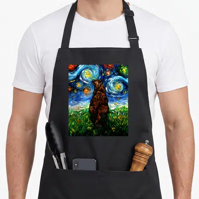 Tortoiseshell kitty cat apron - Brown cat standing in green grass under a swirling blue and yellow starry night sky — shown on a black cotton canvas apron against a white background