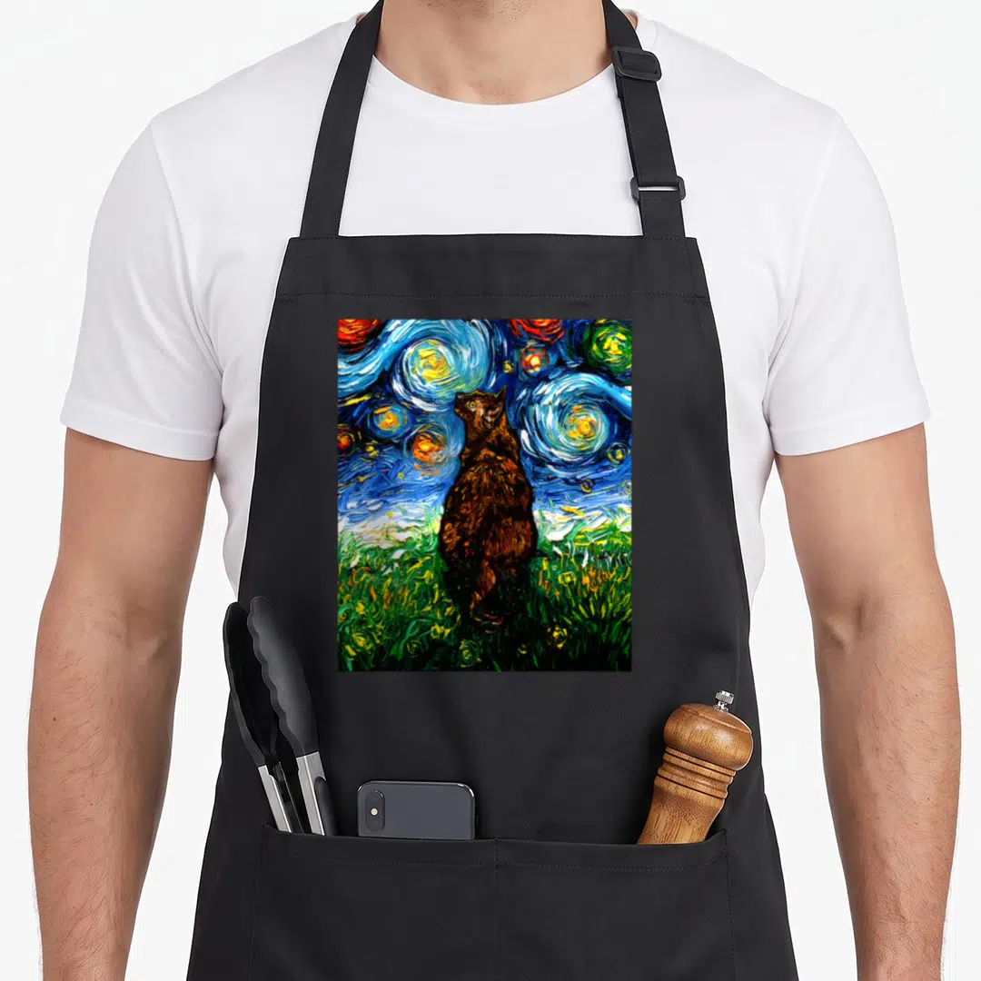Tortoiseshell kitty cat apron - Brown cat standing in green grass under a swirling blue and yellow starry night sky — shown on a black cotton canvas apron against a white background