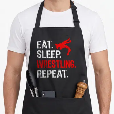 Sleep wrestling apron - Stacked Eat Sleep Wrestling Repeat text with two red wrestlers in action pose — shown on a black cotton canvas apron against a white background