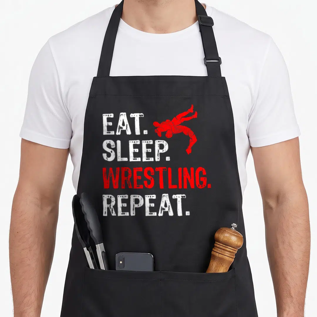 Sleep wrestling apron - Stacked Eat Sleep Wrestling Repeat text with two red wrestlers in action pose — shown on a black cotton canvas apron against a white background