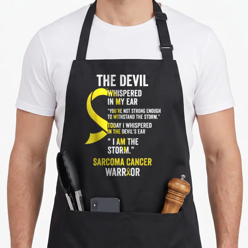 Sarcoma devil's apron - Yellow awareness ribbon with white distressed text reading The Devil Whispered In My Ear — shown on a black cotton canvas apron against a white background