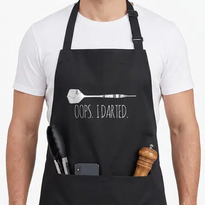 Funny darts apron - White distressed horizontal dart illustration above text OOPS. I DARTED — shown on a black cotton canvas apron against a white background