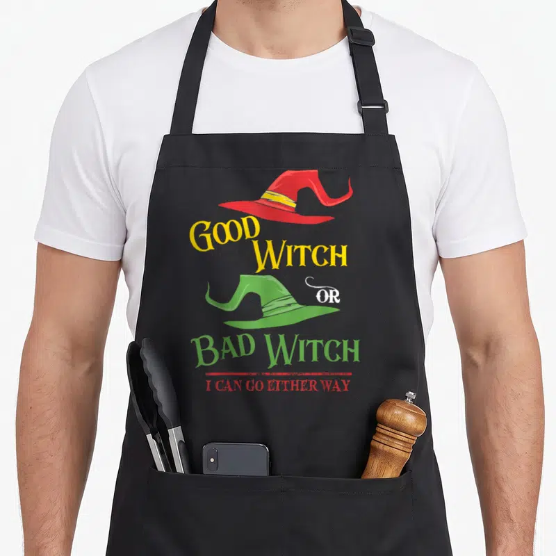 Either halloween witch apron - Red and green witch hats with GOOD WITCH OR BAD WITCH I CAN GO EITHER WAY text — shown on a black cotton canvas apron against a white background