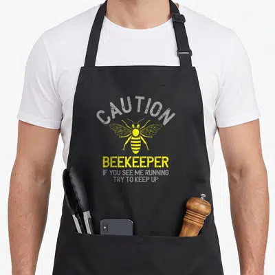 Caution bee apron - Yellow bee graphic with arched caution text and sarcastic running quote in distressed style — shown on a black cotton canvas apron against a white background