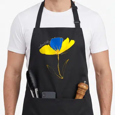 Indomitable ukrainian aprons - Blue and yellow watercolor flower with indomitable script text on black fabric — shown on a black cotton canvas apron against a white background