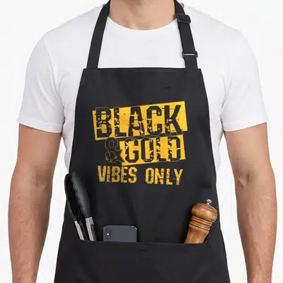Holiday football apron - BLACK & GOLD VIBES ONLY text on yellow rectangular backgrounds in distressed font — shown on a black cotton canvas apron against a white background