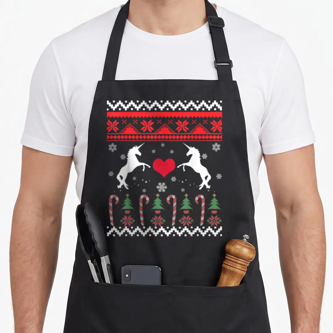 Unicorn ugly sweater apron - Pixelated unicorns, red heart, candy canes, Christmas trees, snowflakes, white and red — shown on a black cotton canvas apron against a white background