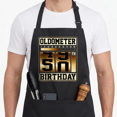 Oldometer father day apron - Gold and black 50th birthday odometer typography design enclosed in a rounded frame — shown on a black cotton canvas apron against a white background