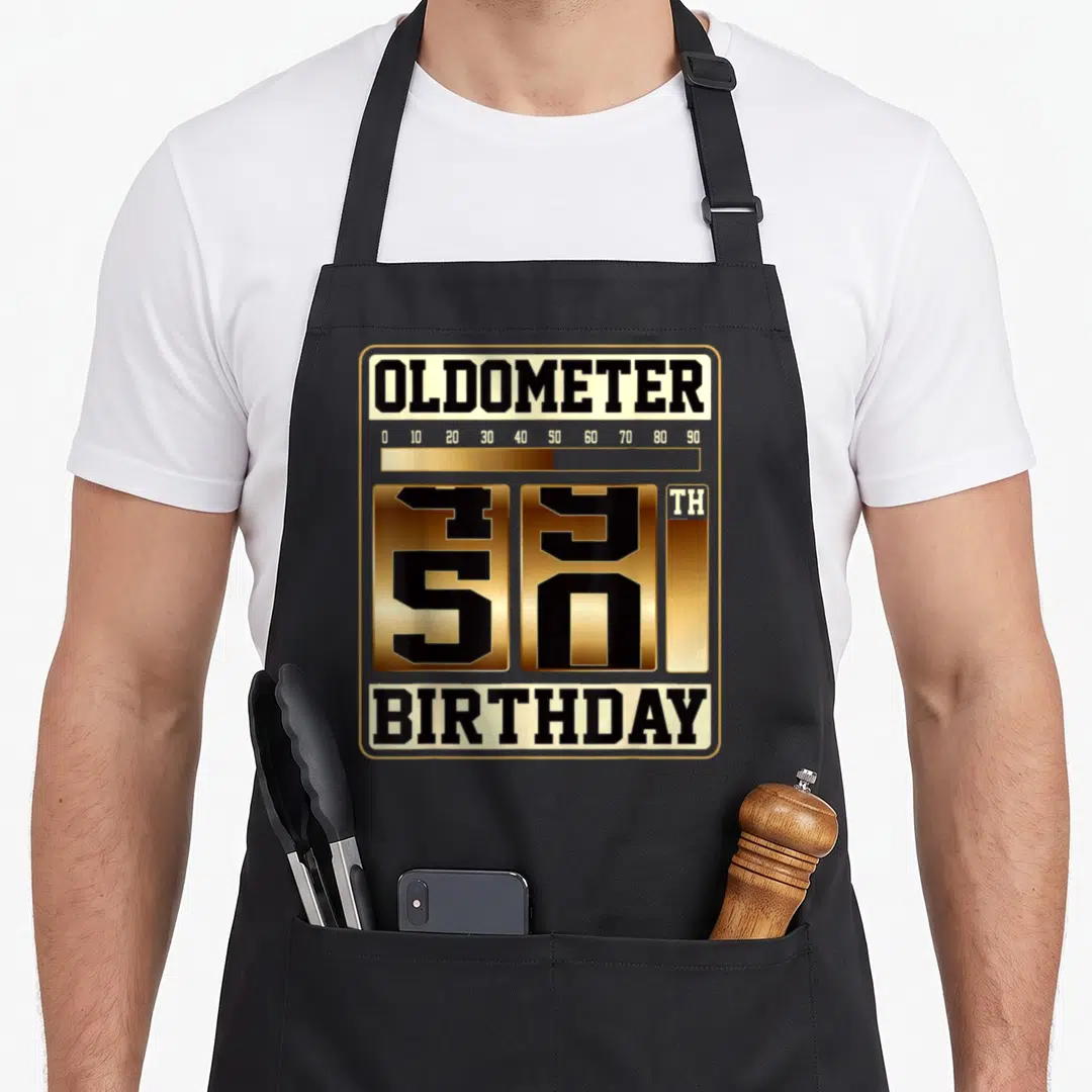 Oldometer father day apron - Gold and black 50th birthday odometer typography design enclosed in a rounded frame — shown on a black cotton canvas apron against a white background
