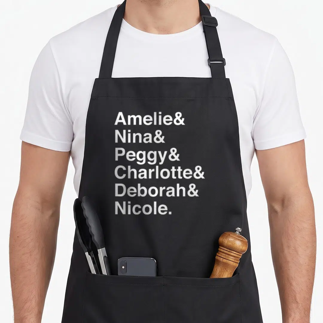 Techno dj apron - White stacked text reading Amelie Nina Peggy Charlotte Deborah Nicole — shown on a black cotton canvas apron against a white background