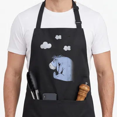 Cloud eeyore apron - Blue cartoon donkey sitting under three grey clouds with bottom attribution text — shown on a black cotton canvas apron against a white background