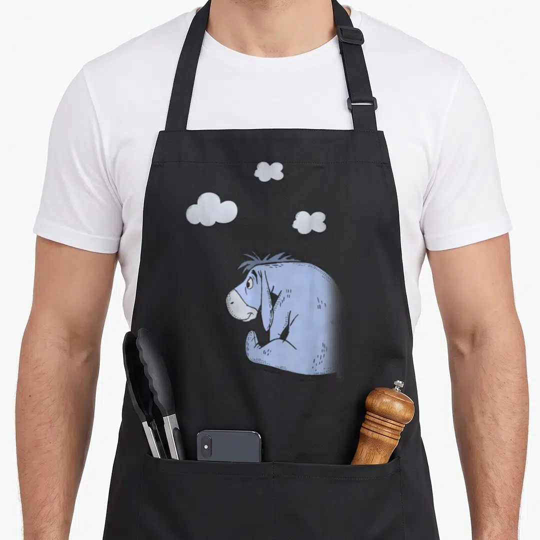 Cloud eeyore apron - Blue cartoon donkey sitting under three grey clouds with bottom attribution text — shown on a black cotton canvas apron against a white background