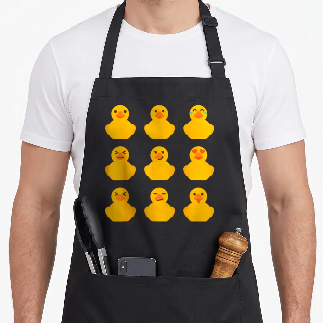 Ducky duck apron - Nine yellow cartoon ducks with varied facial expressions in a grid pattern — shown on a black cotton canvas apron against a white background