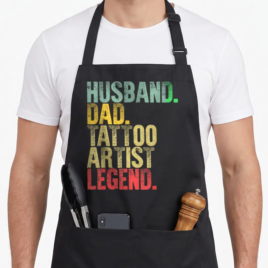 Husband tattoo aprons - Stacked text HUSBAND DAD TATTOO ARTIST LEGEND in green yellow beige red vintage font — shown on a black cotton canvas apron against a white background