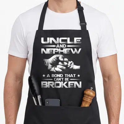 Bond nephew apron - Fist bump between adult and baby hands with text UNCLE AND NEPHEW A BOND THAT CAN'T BE BROKEN — shown on a black cotton canvas apron against a white background