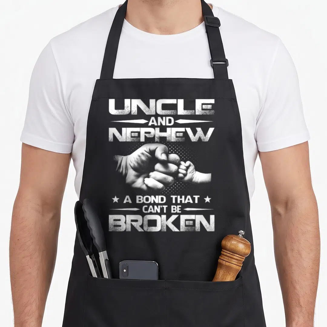 Bond nephew apron - Fist bump between adult and baby hands with text UNCLE AND NEPHEW A BOND THAT CAN'T BE BROKEN — shown on a black cotton canvas apron against a white background