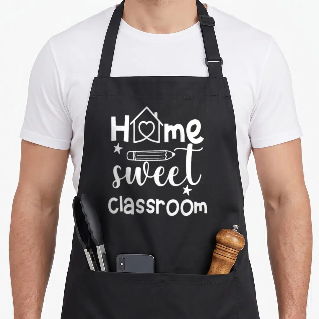 Sweet school classroom aprons - White stacked text Home Sweet Classroom with pencil and heart house icon — shown on a black cotton canvas apron against a white background
