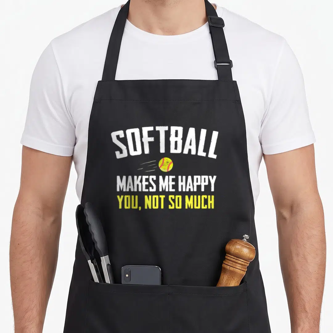 Cool softball apron - Stacked white and yellow text SOFTBALL MAKES ME HAPPY YOU NOT SO MUCH with a yellow ball — shown on a black cotton canvas apron against a white background