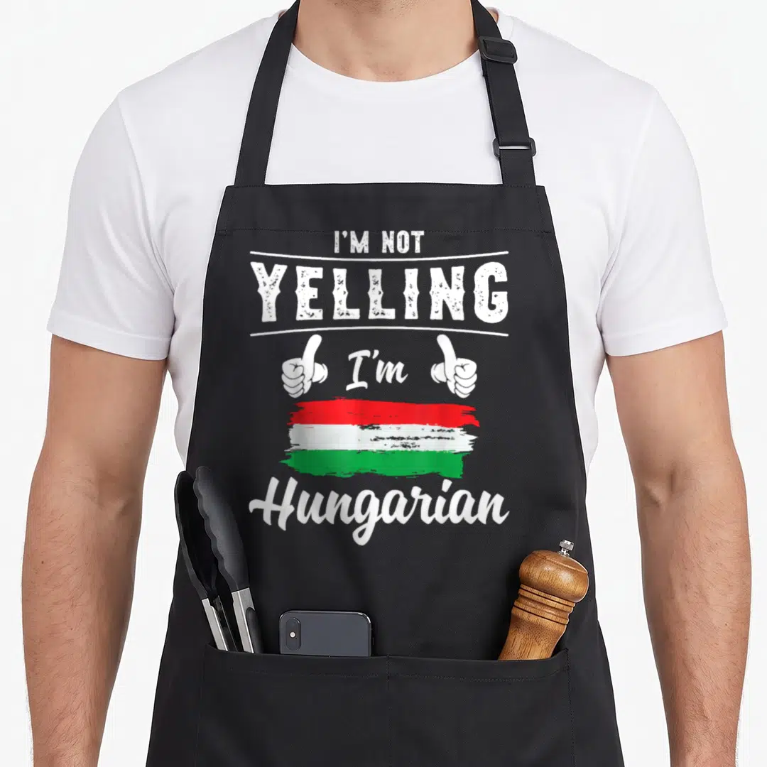 Hungarian pride apron - I'm Not Yelling text with thumbs up and red white green flag stripes — shown on a black cotton canvas apron against a white background