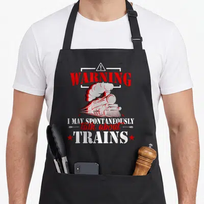 Warning train apron - Red and white steam locomotive graphic with warning text and stars flanking the bottom line — shown on a black cotton canvas apron against a white background
