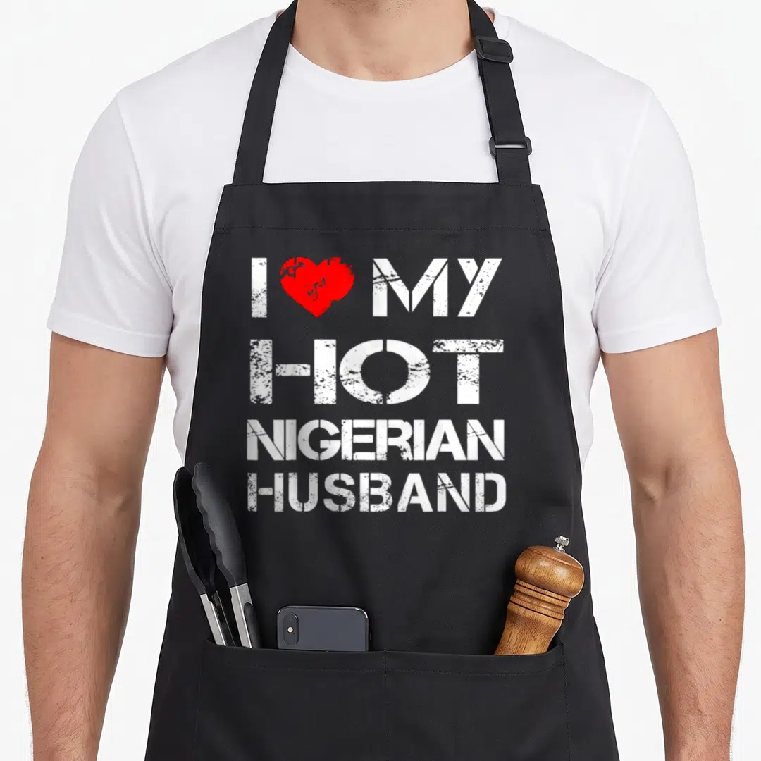 Nigerian husband wife aprons - White stacked text I MY HOT NIGERIAN HUSBAND with red heart on black bib — shown on a black cotton canvas apron against a white background