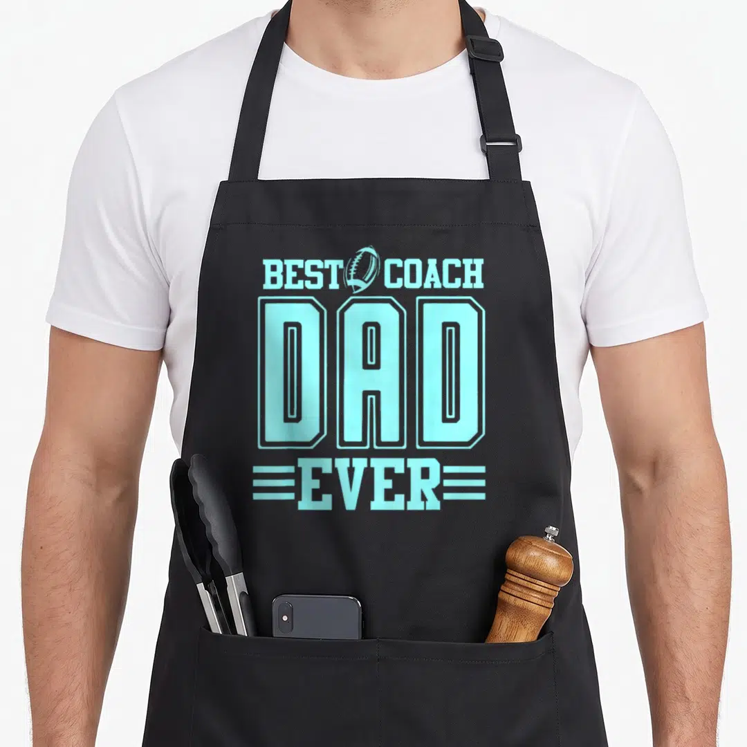 Coach football father day apron - Light blue text reading Best Coach Dad Ever with football and three horizontal lines — shown on a black cotton canvas apron against a white background