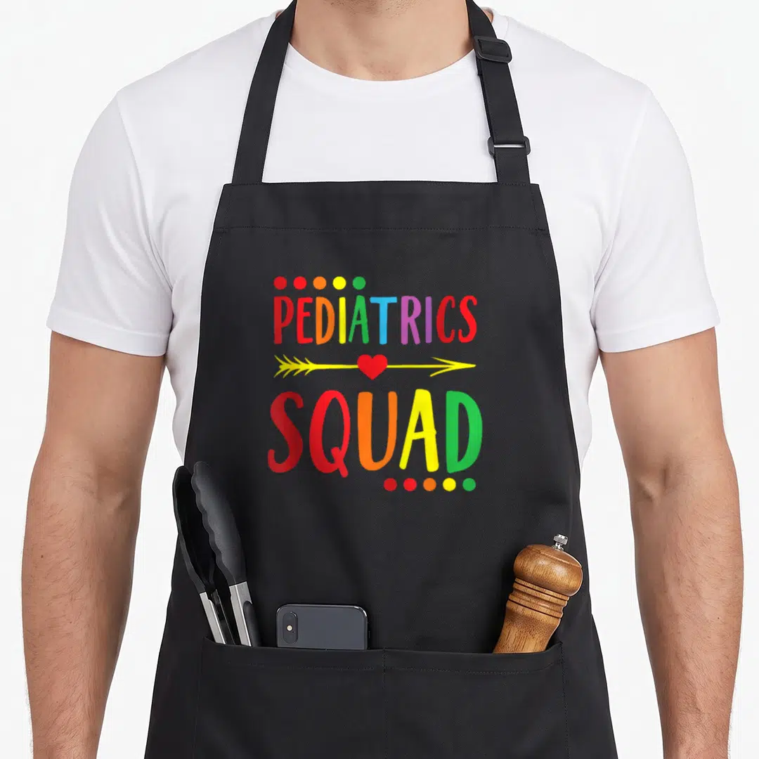 Ped nurse apron - PEDIATRICS SQUAD text with yellow arrow red heart and colored circles — shown on a black cotton canvas apron against a white background