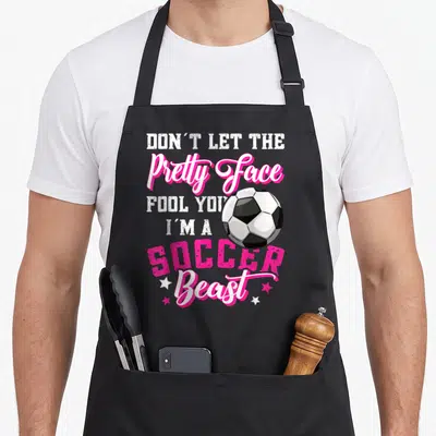 Soccer pretty apron - Stacked pink and white text reading Don't Let The Pretty Face Fool You I'm A Soccer Beast — shown on a black cotton canvas apron against a white background