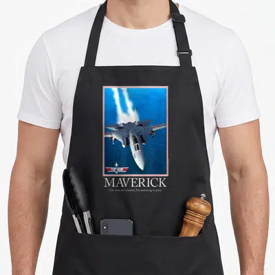 Motivational gun apron - Fighter jet over blue ocean with red border and text Top Gun Maverick Too close for missiles — shown on a black cotton canvas apron against a white background