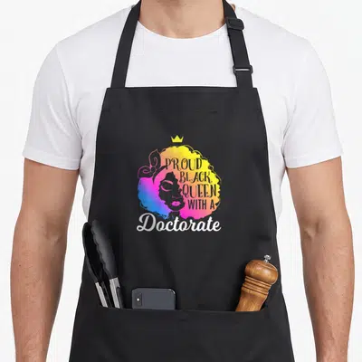 Doctorate queen apron - Gradient woman silhouette with crown and PROUD BLACK QUEEN WITH A Doctorate text — shown on a black cotton canvas apron against a white background