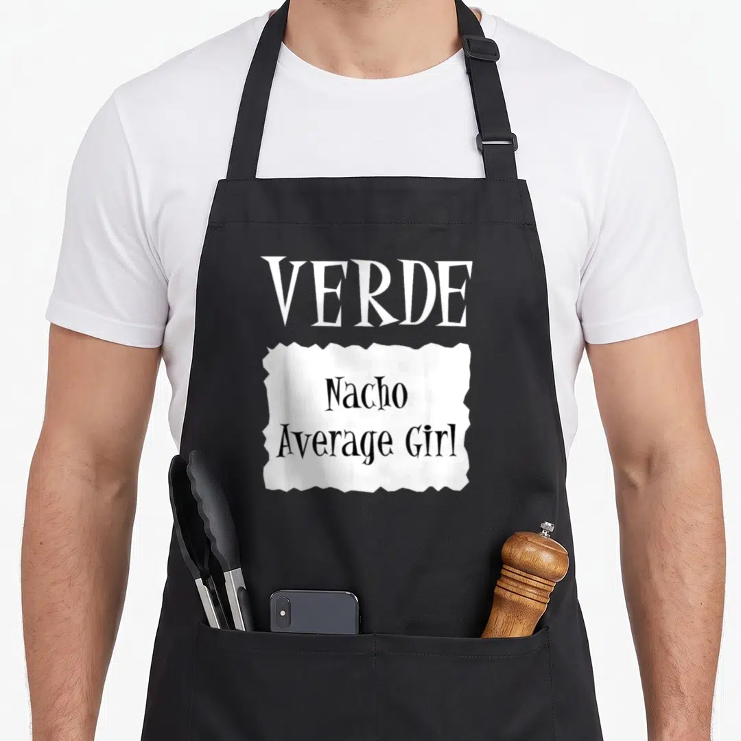 Halloween taco apron - White VERDE text above a torn paper graphic reading Nacho Average Girl in black — shown on a black cotton canvas apron against a white background