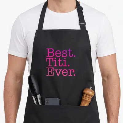 Titi spanish aprons - Stacked pink and purple text reading Best Titi Ever on black fabric — shown on a black cotton canvas apron against a white background