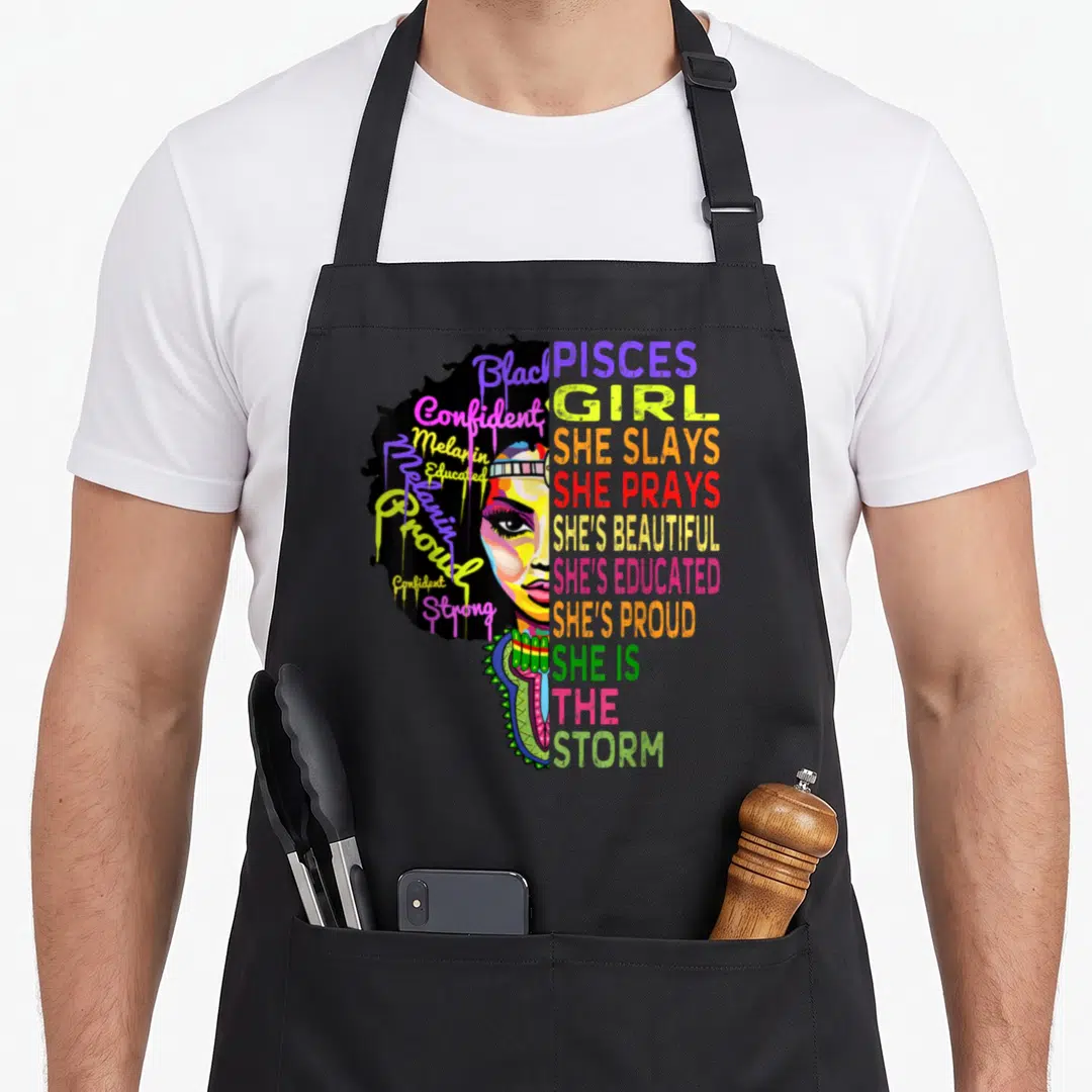 She birthday apron - Split face portrait with colorful stacked text Pisces Girl She Slays Prays Beautiful Educated — shown on a black cotton canvas apron against a white background