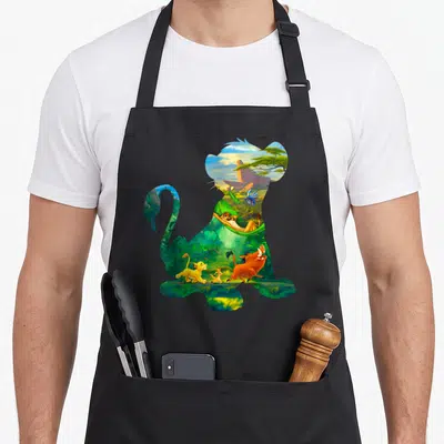 Simba lion apron - Sitting lion silhouette containing a cartoon jungle scene with running characters in green and orange — shown on a black cotton canvas apron against a white background
