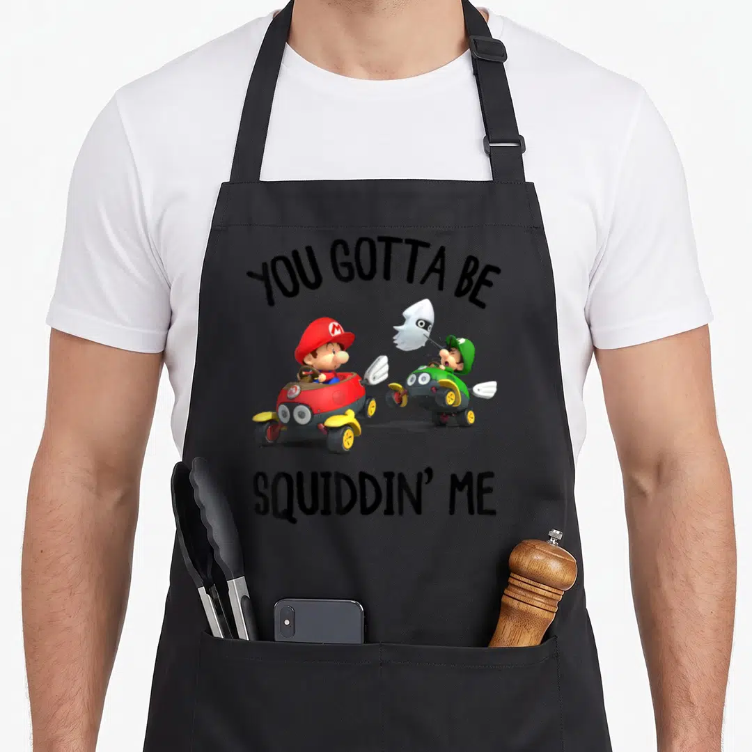 Squiddin novelty apron - Mario and Luigi in karts chased by ghost with You Gotta Be Squiddin Me text — shown on a black cotton canvas apron against a white background