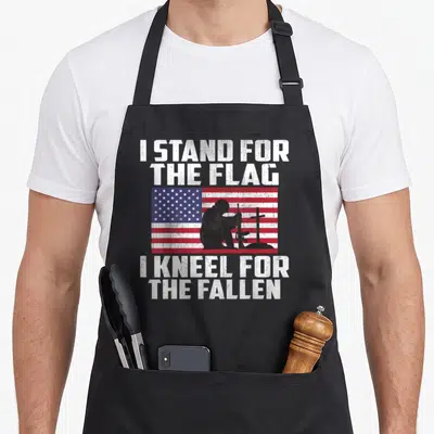 Stand memorial apron - I Stand For The Flag I Kneel For The Fallen text with kneeling soldier silhouette over USA flag — shown on a black cotton canvas apron against a white background