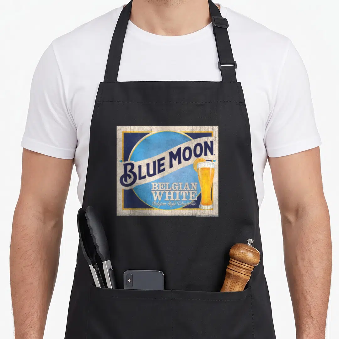 Coor moon retro apron - Blue Moon Belgian White logo with beer glass and orange slice on light blue circle — shown on a black cotton canvas apron against a white background