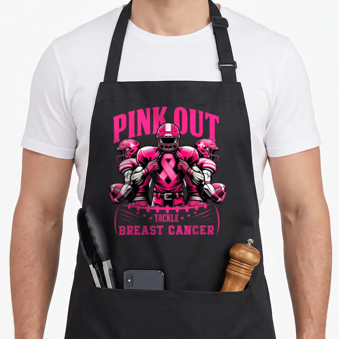 Tackle ribbon apron - Three cartoon football players in pink with large ribbon on chest and tackle breast cancer text — shown on a black cotton canvas apron against a white background