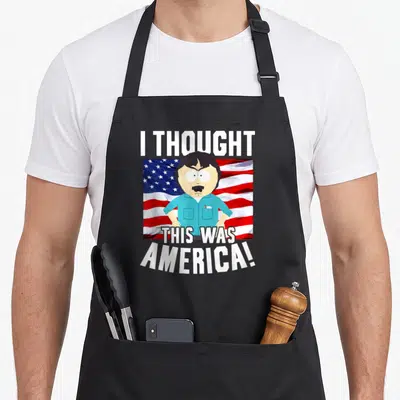 Randy cartoon apron - Cartoon man centered on waving flag with white text reading I thought this was america — shown on a black cotton canvas apron against a white background