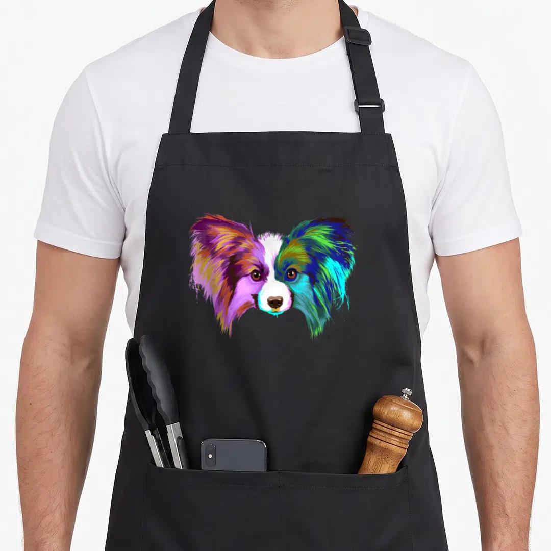 Colourful papillon dog apron - Multicolored cartoon Papillon dog head with purple blue green pink and white fur — shown on a black cotton canvas apron against a white background